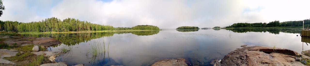 Järvimaisema, jossa etualalla kallioita ja takana kohoaa kuusimetsää.